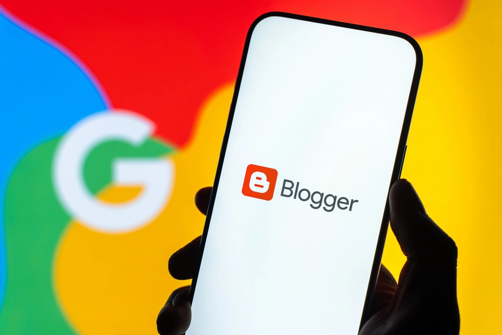 Logo Bloggera, znanego jako Blogspot, na ekranie smartfona na tle kolorowego logo Google