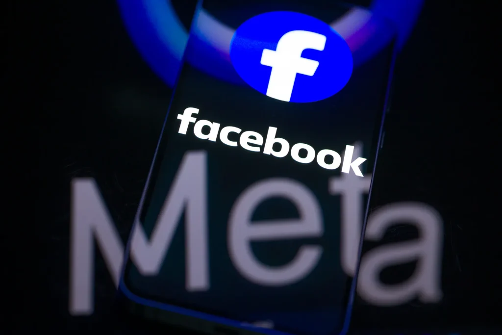 Facebook na smartfonie na tle logo Meta. Źródło: Adobe Stock